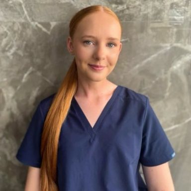 A woman with long red hair wearing a navy medical scrubs top.